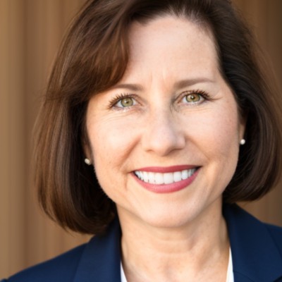 Close-up portrait of a smiling woman with short brown hair wearing a navy blazer.