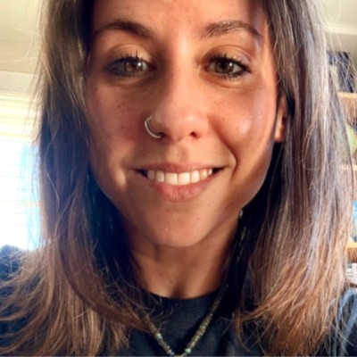 Close-up of a woman with a nose ring smiling at the camera indoors.